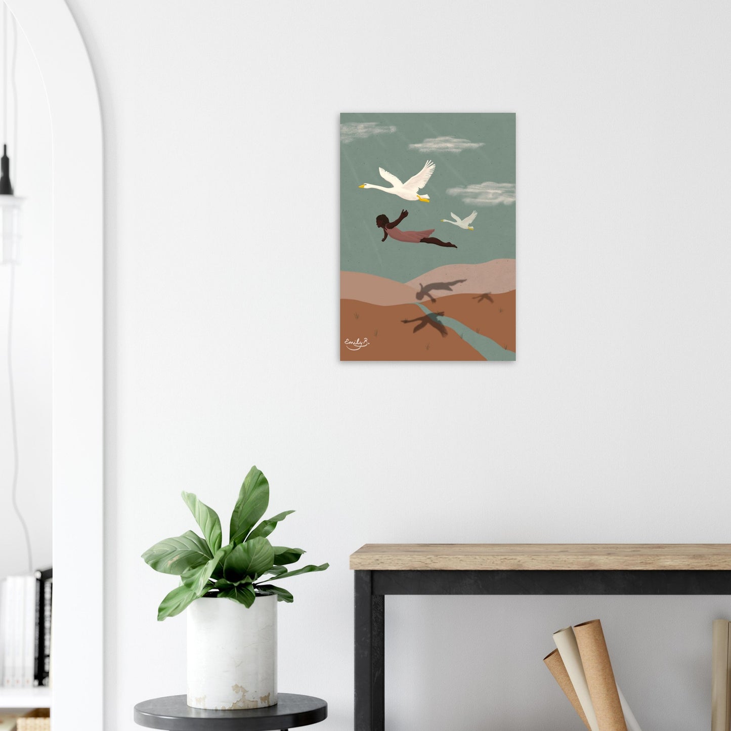 Flying With Swans art print displayed in a modern interior, showing a Black woman in a pink dress gliding above rolling terracotta hills with two swans and long shadows